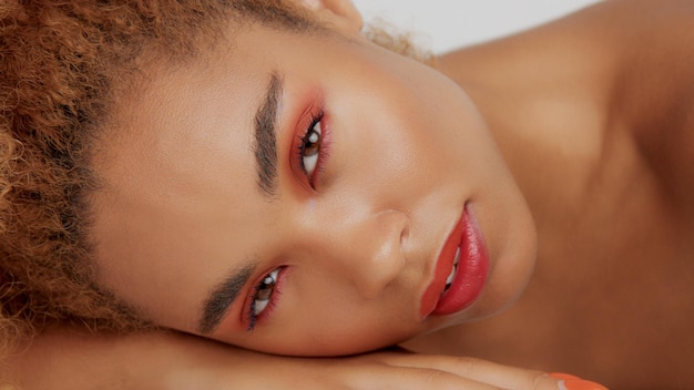 Bezpłatne zdjęcie zbliżenie rasy mieszanej czarna kobieta z czerwonym makijażem w pozycji leżącej na własnej ręce