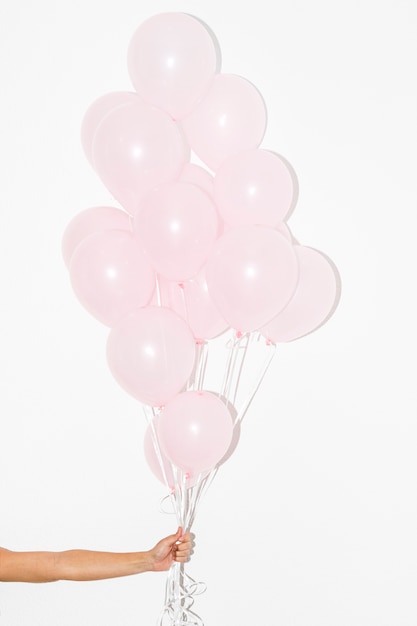 Zbliżenie ręki trzymającej bukiet różowych balonów na białym tle