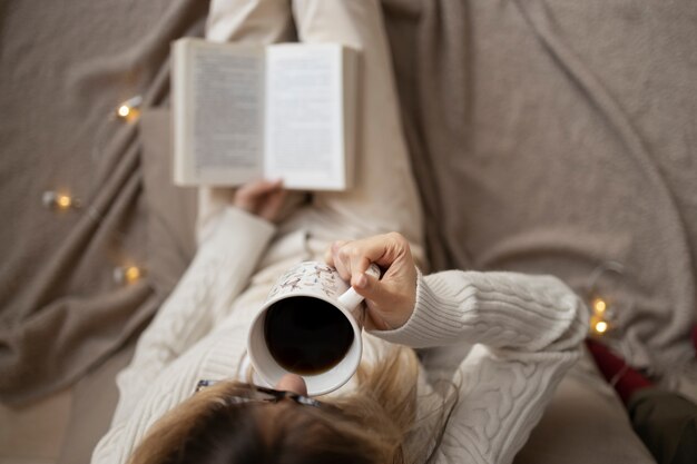 Zbliżenie ręki trzymającej książkę i filiżankę kawy