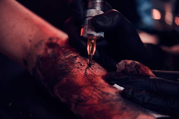 Zbliżenie sesji zdjęciowej tatuażu, artysta pracuje z maszynką do tatuażu na rękę klienta.