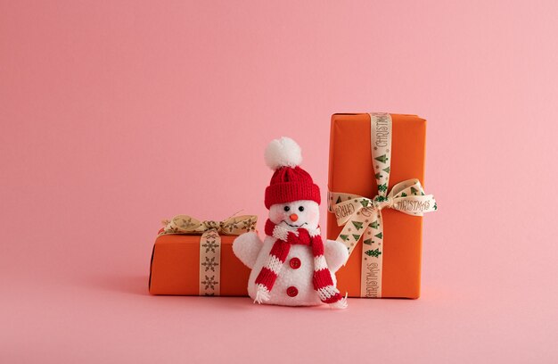 Zbliżenie śmiesznego bałwana i pomarańczowych pudełek na prezenty na różowym tle