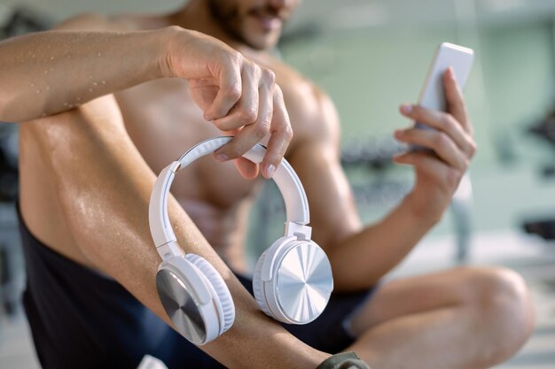 Zbliżenie sportowca trzymającego słuchawki podczas korzystania ze smartfona w siłowni