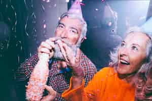 Bezpłatne zdjęcie zbliżenie starszy mężczyzna trzyma butelkę szampana i jej żona rzuca konfetti w powietrzu na przyjęcie urodzinowe
