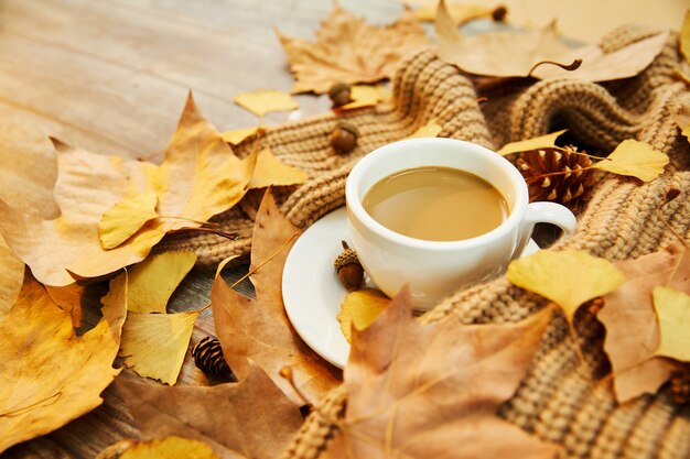 Zbliżenie strzał filiżanki kawy i jesiennych liści na drewnianym tle