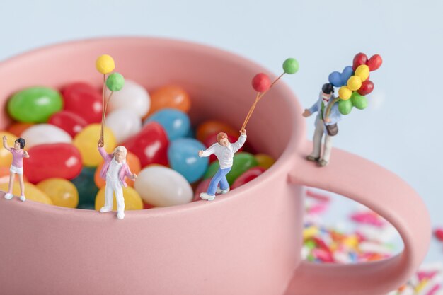 Zbliżenie strzał postaci ludzi z balonami na filiżance z kolorowymi cukierkami