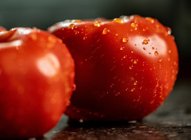 Zbliżenie świeżych dojrzałych pomidorów z kroplami wody na powierzchni blatu kuchni czarnego granitu