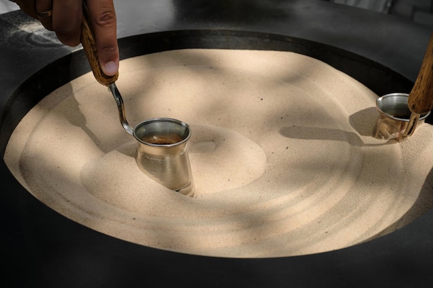 Zbliżenie tureckiej kawy w cezve na piasku w kawiarni Profesjonalny barista ręcznie przygotowuje kawę w tradycyjny sposób przy użyciu nowoczesnego sprzętu Selektywna przestrzeń ostrości dla tekstu