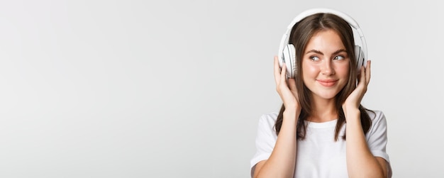 Zbliżenie uśmiechnięta atrakcyjna brunetka dziewczyna słucha muzyki w słuchawkach ciesząc się ciekawym podca