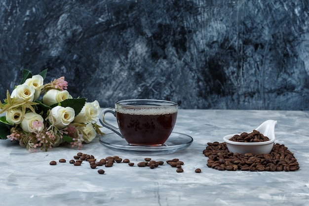 Zbliżenie ziarna kawy w dzbanku z białej porcelany z filiżanką kawy, kwiaty na granatowym i jasnoniebieskim tle marmuru. poziomy