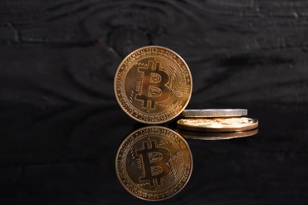 Zbliżenie złotego bitcoina na ciemnej, odbijającej światło powierzchni i histogram malejącego krypto