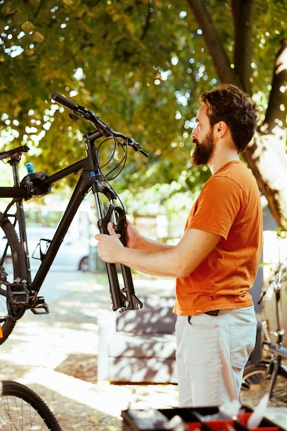 Zdecydowany młody aktywny mężczyzna delikatnie dostosowuje przedni widelec i zestaw słuchawkowy do bezpiecznego jazdy na rowerze na świeżym powietrzu.