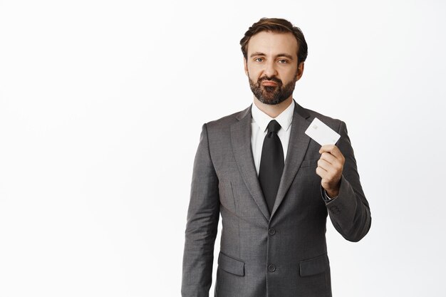Zdenerwowany biznesmen pokazujący kartę kredytową i krzywiący się, stojący na białym tle