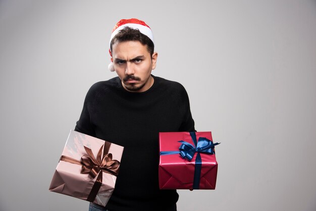 Zdenerwowany mężczyzna w czapce Świętego Mikołaja trzymający prezenty noworoczne.