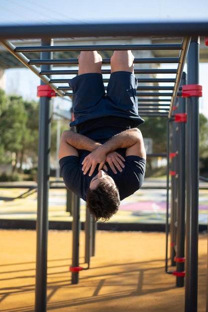 Zdeterminowany sportowiec ćwiczący w słoneczny dzień. Mężczyzna sportive ubrania na boisku sportowym na świeżym powietrzu, podciągając się na barach. Sport, zdrowie, opracowanie koncepcji