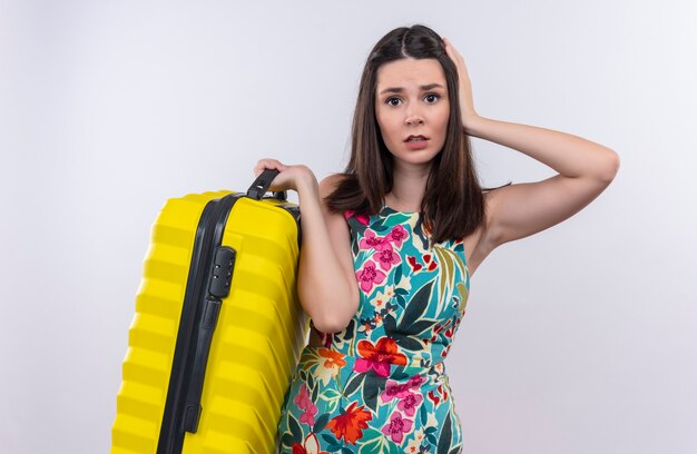 Zdezorientowana młoda podróżniczka kobieta trzyma walizkę stojącą nad izolowaną białą ścianą