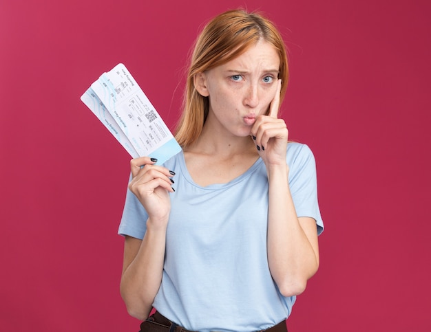 Bezpłatne zdjęcie zdezorientowana młoda rudowłosa dziewczyna z piegami trzymająca bilety lotnicze