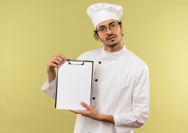 zdezorientowany młody kucharz mężczyzna ubrany w mundur szefa kuchni i okulary trzymając schowek