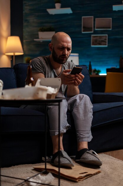 Zdezorientowany, niespokojny mężczyzna patrzący na ekran smartfona, przeglądający internet, by zapomnieć o problemach ze zdrowiem psychicznym i przewlekłej depresji. Dorosły z depresją samobójczą z technologią mobilną.