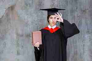 Bezpłatne zdjęcie zdjęcie inteligentnego absolwenta pokazującego jej książkę dyplomową przez ścianę. zdjęcie wysokiej jakości