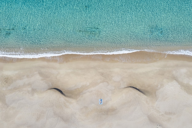 Zdjęcie lotnicze osoby leżącej na piaszczystej plaży w pobliżu morza