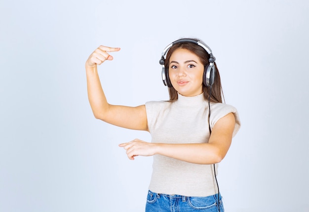 Zdjęcie Modelu Młoda Kobieta Słuchania Muzyki W Słuchawkach I Wskazując Na Bok Palcami Wskazującymi.