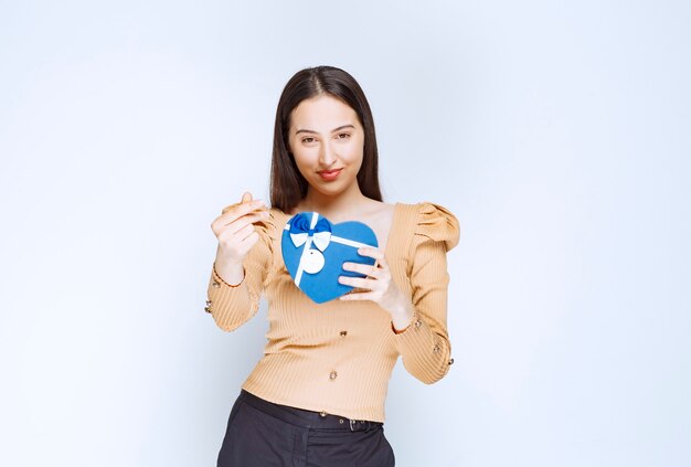 Zdjęcie modelu młoda kobieta trzyma pudełko w kształcie serca na białej ścianie.