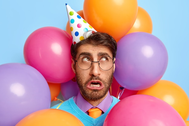 Zdjęcie nieszczęśliwego faceta otoczonego przez balony imprezowe pozowanie