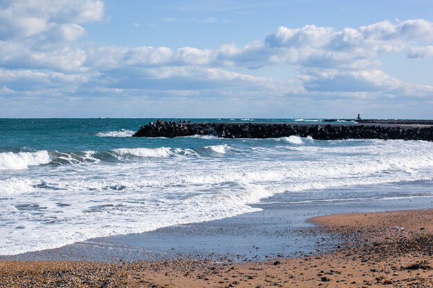 Zdjęcie relaksujących fal oceanu na brzegu z kamiennym pomostem pod zachmurzonym niebem