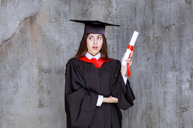 Bezpłatne zdjęcie zdjęcie studentki w sukni pozującej ze świadectwem ukończenia szkoły. zdjęcie wysokiej jakości