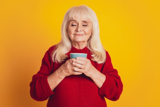 Zdjęcie uroczej starszej pani w podeszłym wieku pijącej kakao pachnące smakiem na żółtym tle