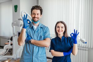 Bezpłatne zdjęcie zdjęcie uśmiechniętego dentysty stojącego z rękami skrzyżowanymi z kolegą, pokazującego znak porządku.