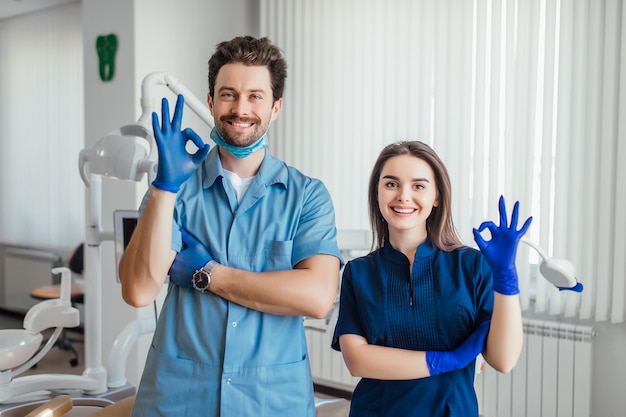 Zdjęcie uśmiechniętego dentysty stojącego z rękami skrzyżowanymi z kolegą, pokazującego znak porządku.