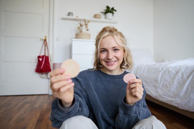 Zdjęcie uśmiechniętej blondynki vlogger pokazującej produkty makijażowe elementy piękności zalecane dla obserwujących