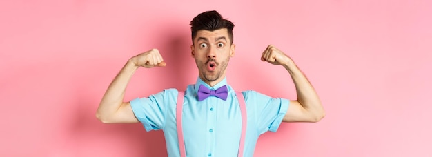 Bezpłatne zdjęcie zdjęcie zabawnego faceta z wąsami i muszką, pokazującego mięśnie napinające bicepsy i wyglądającego na zaskoczonego