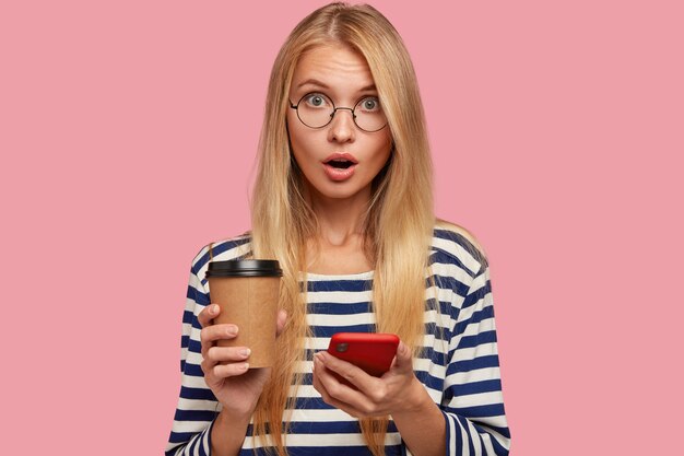 Zdjęcie zdziwionej blondynki młodej kobiety z zaskoczonym wyrazem twarzy, używa telefonu komórkowego