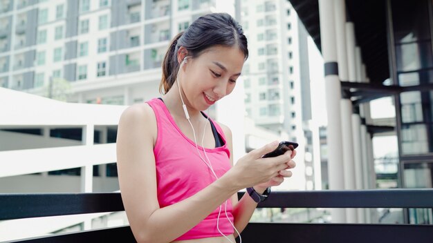 Zdrowa piękna młoda Azjatycka atleta kobieta używa smartphone dla słucha muzyka podczas gdy biegający