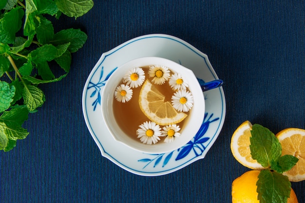 Zdrowa rumianek herbata z cytrynami i liśćmi w filiżance i kumberlandzie na ciemnym podkładki tle, zakończenie.
