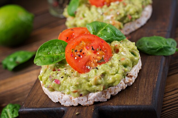 Bezpłatne zdjęcie zdrowe śniadanie. kanapka chrupiący chleb z guacamole i pomidorami na drewnianym stole.