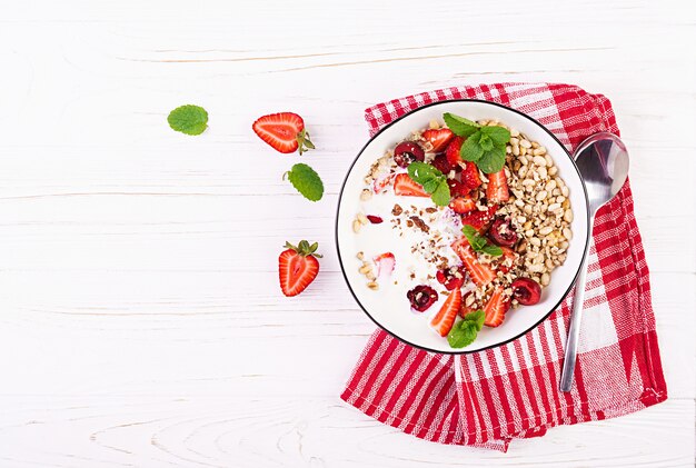 Zdrowe śniadanie - muesli, truskawek, wiśni, orzechów i jogurtu w misce na drewnianym stole. Wegetariańskie jedzenie koncepcja. Widok z góry