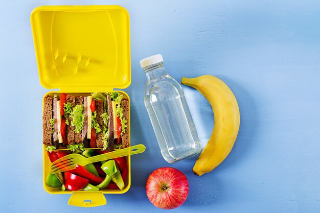 Zdrowe szkolne pudełko na lunch z kanapką wołową i świeżymi warzywami, butelką wody i owoców