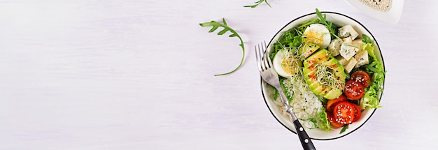 Zdrowy zielony wegetariański lunch miska Buddy z jajkami, ryżem, pomidorem, awokado i serem pleśniowym na stole.