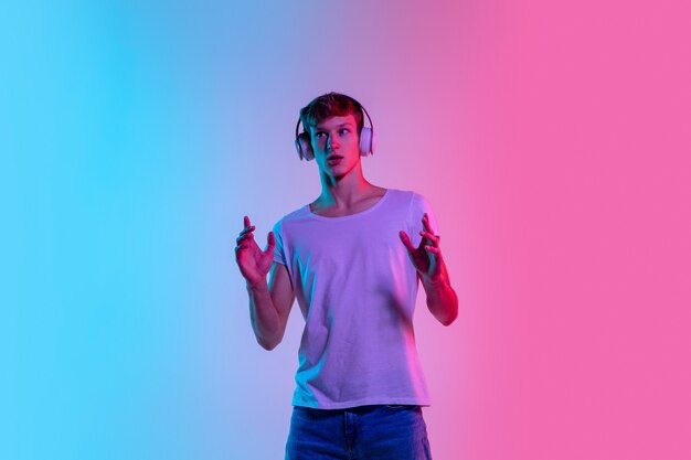 Zdumiony. Portret młodego mężczyzny kaukaski na tle gradientu niebiesko-różowy studio w świetle neonu. Pojęcie młodości, ludzkie emocje, wyraz twarzy, sprzedaż, reklama. Piękny model na co dzień.