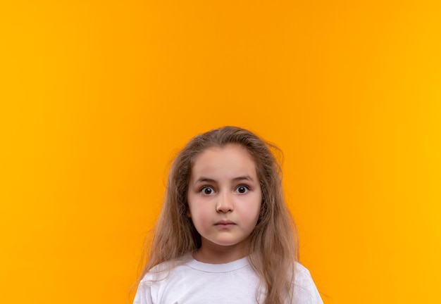 Zdziwiona mała uczennica ubrana w białą koszulkę na na białym tle pomarańczowym tle