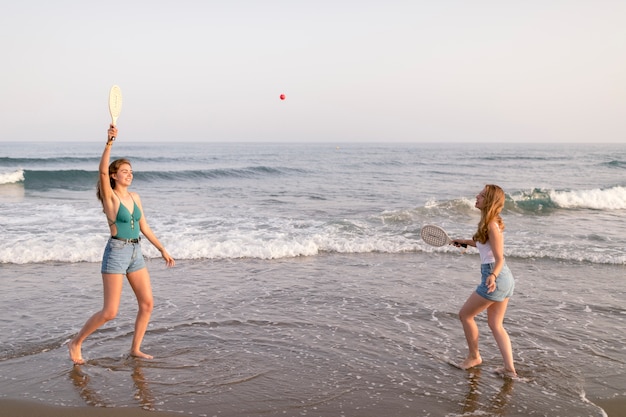 Żeńscy przyjaciele cieszy się bawić się z tenisem przy seashore