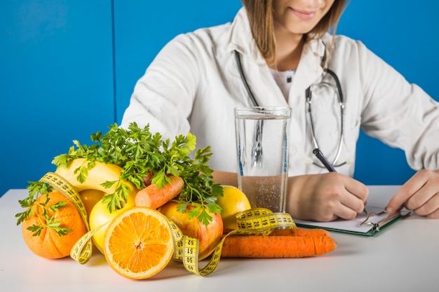 Bezpłatne zdjęcie Żeński dietician writing na schowku z świeżymi owoc na biurku