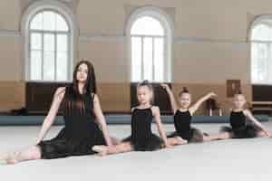 Bezpłatne zdjęcie Żeński instruktor siedzi z trzy dziewczynami na podłoga w klasy taneczne