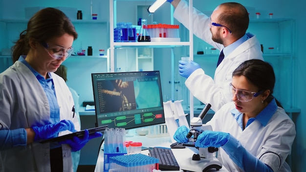Zespół pozytywnych naukowców pracujących w laboratorium wyposażonym w chemię, pielęgniarka pisząca na tablecie