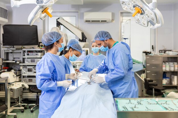 Zespół profesjonalnych lekarzy wykonujących operację na sali operacyjnej Zespół medyczny wykonujący operację chirurgiczną w Jasnej Nowoczesnej Sali Operacyjnej