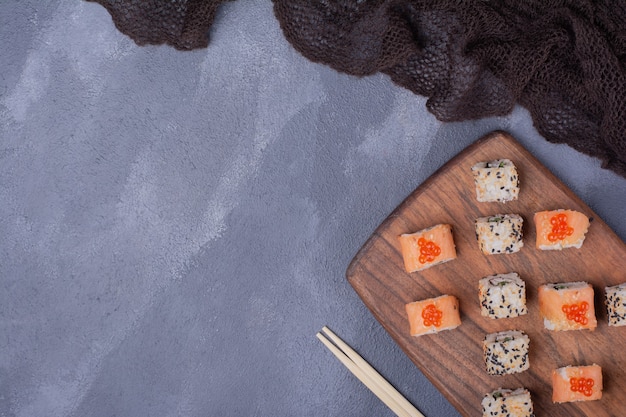 Bezpłatne zdjęcie zestaw do sushi. filadelfia i alaska toczą się na drewnianym talerzu z pałeczkami.