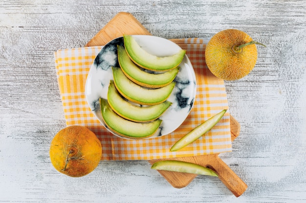 Zestaw melonów i plastry melona w talerzu na teksturowanej szmatką i białym tle kamienia. leżał płasko.